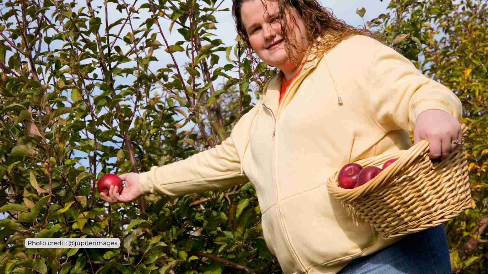 PLus sized woman holding basket of apples in field